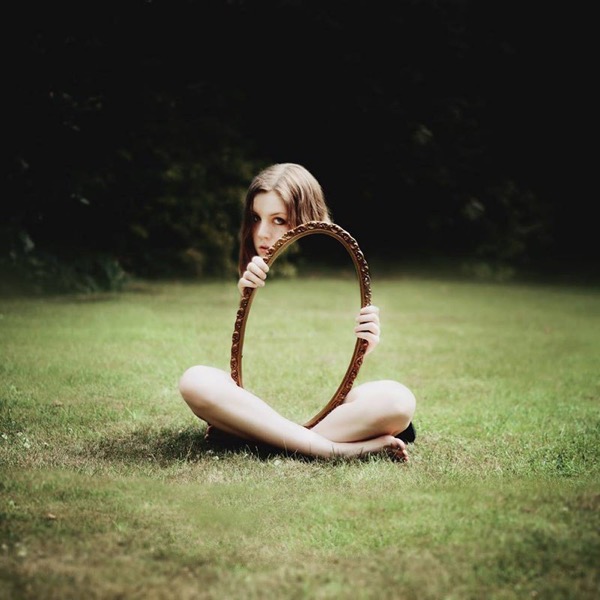 Woman holding mirror on grass reflection